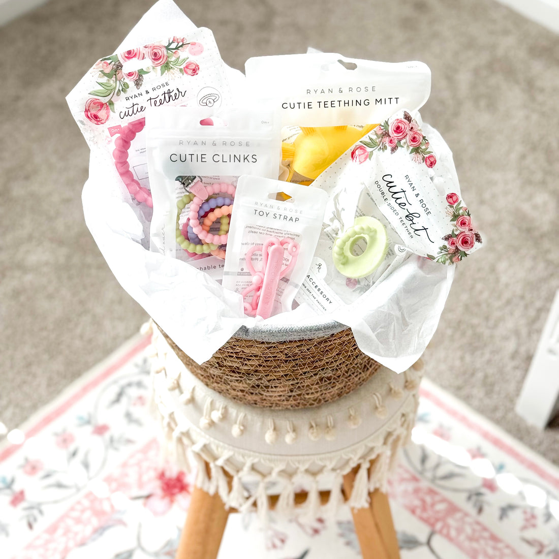 Collection of baby products including teething toys and mitts on a stool with a floral pattern.