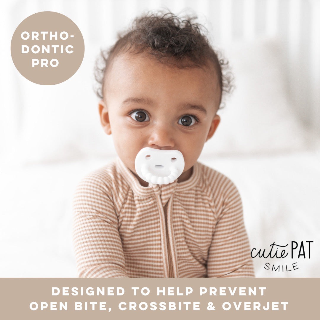 Baby using White Cutie PAT Smile. An orthodontic pro pacifier designed to help prevent open bite, crossbite &amp; overjet.