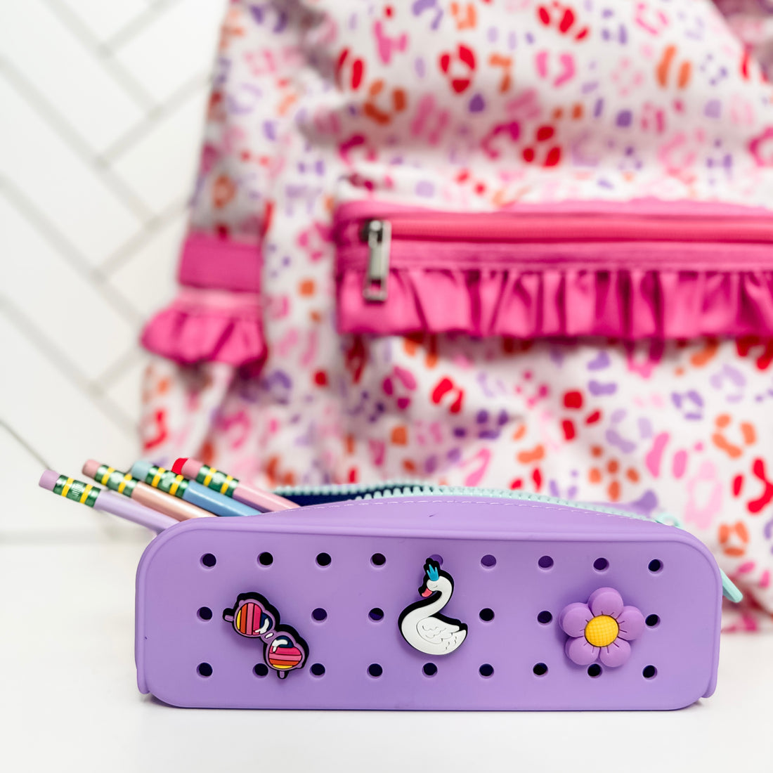 Purple pencil case with decorative elements in front of a colorful backpack.