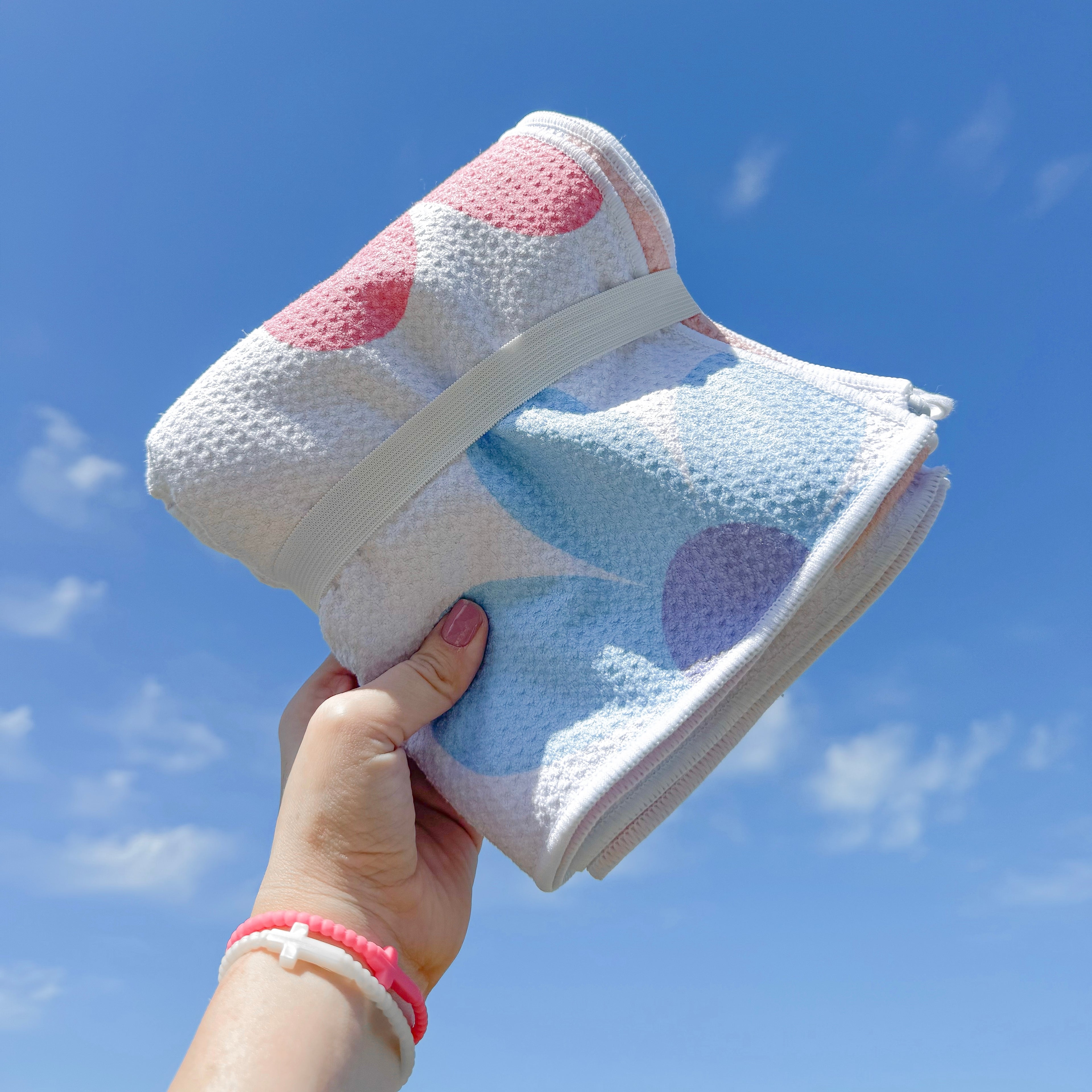 Hand holding a colorful polka dot towel against a blue sky