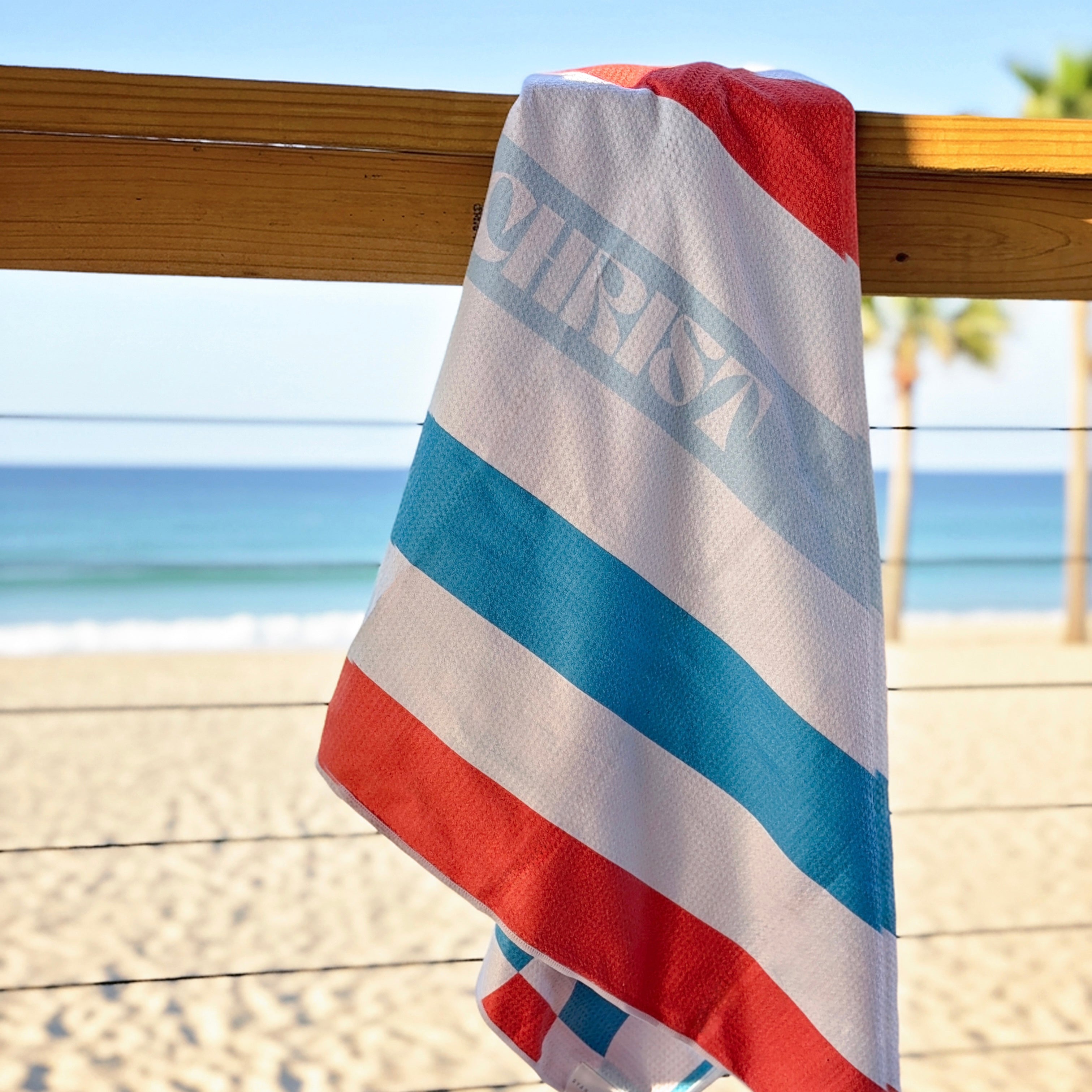 Striped beach towel on a wooden railing by the beach.