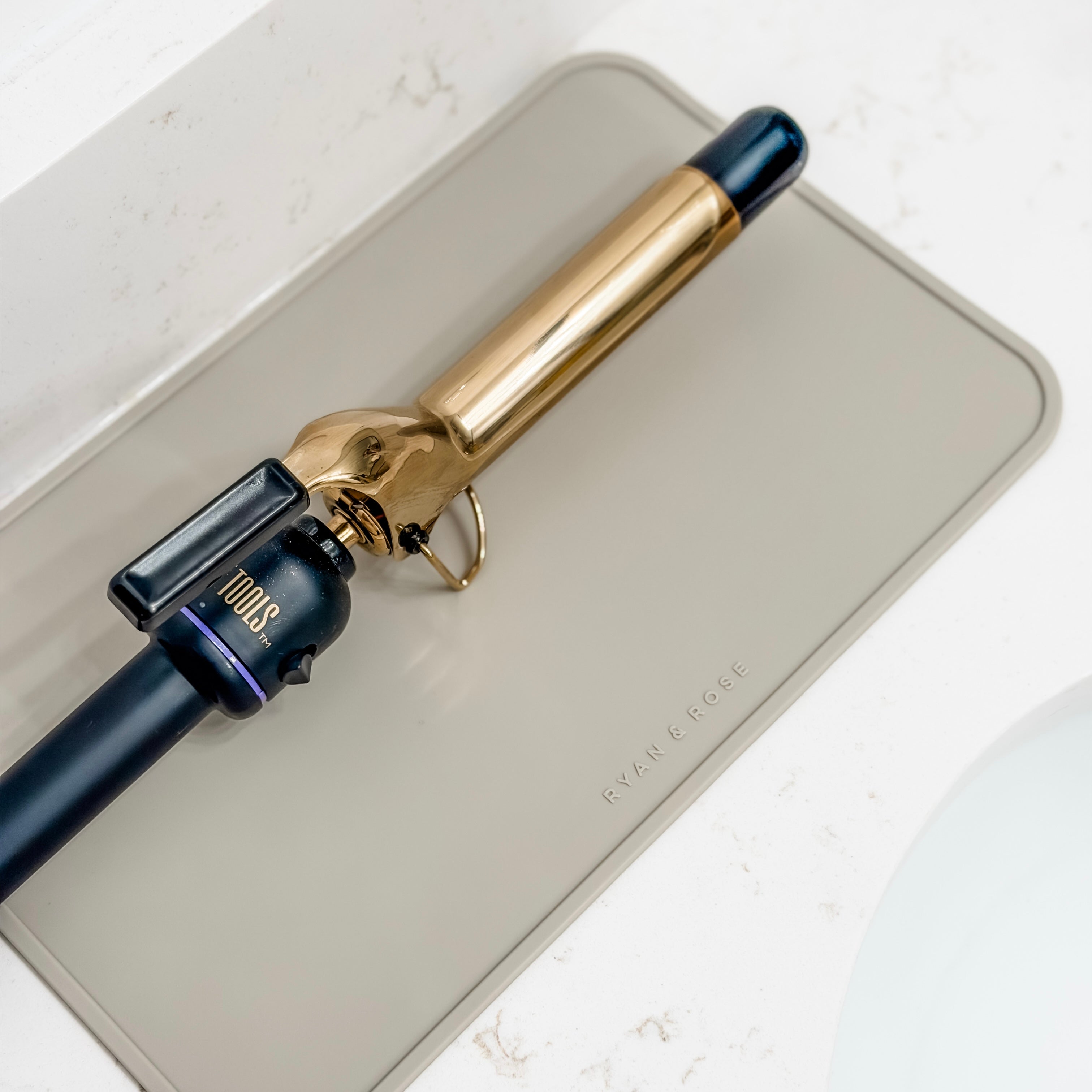 Gold and black curling iron on a beige mat with &