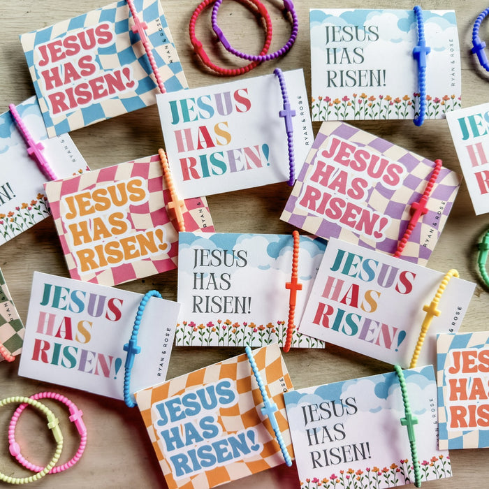 Colorful 'Jesus Has Risen!' cards with bracelets on a wooden surface