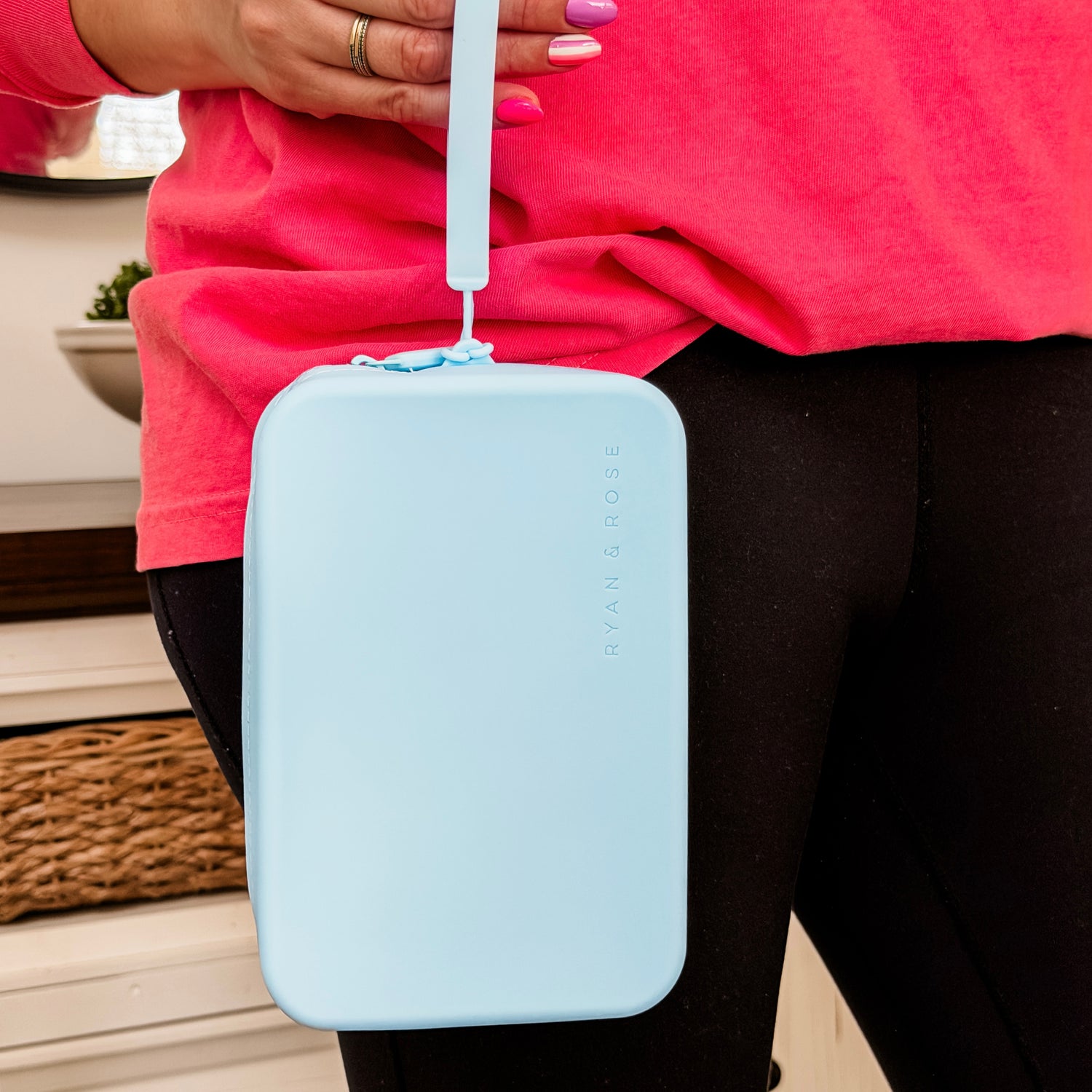Light blue rectangular pouch with a strap held by a person wearing a pink shirt and black pants.