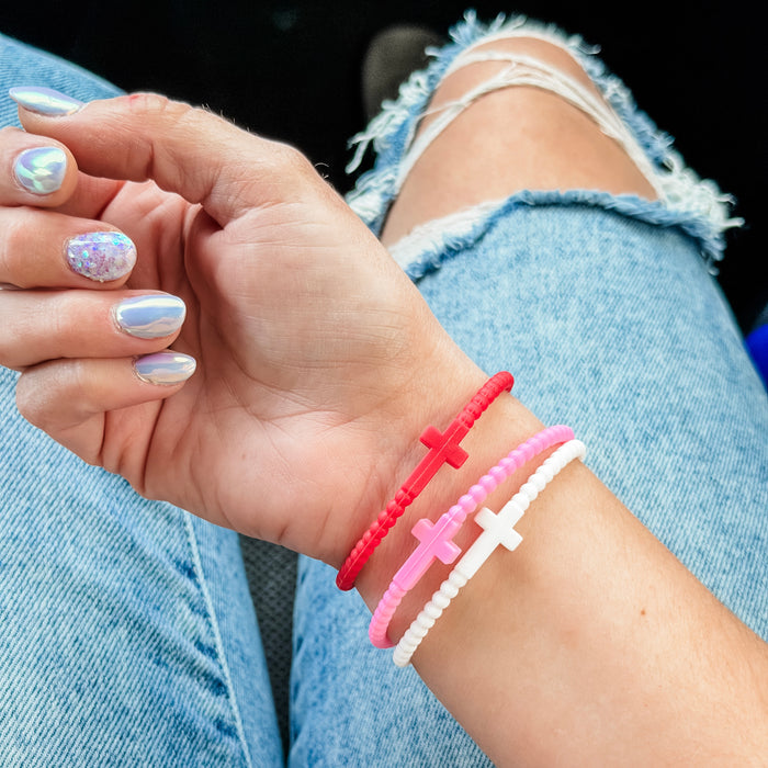 Hand with colorful nail polish wearing three cross-shaped bracelets on a denim background
