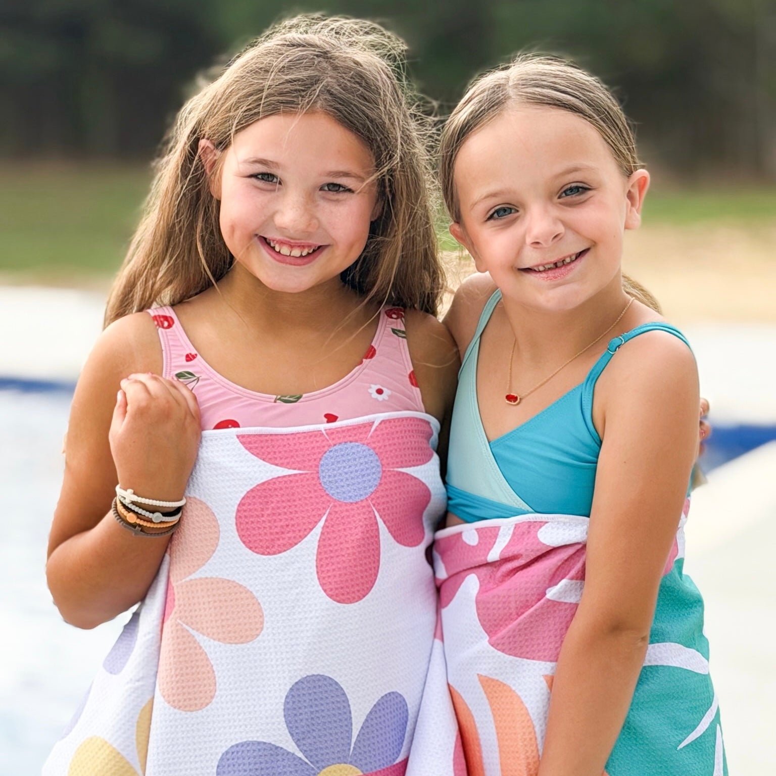 Two young girls wearing colorful swimsuits standing close together outdoors.