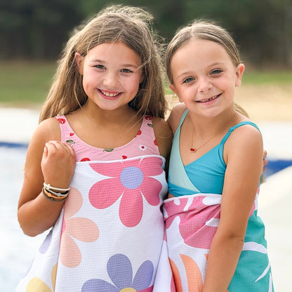 Two young girls wearing colorful swimsuits standing close together outdoors.