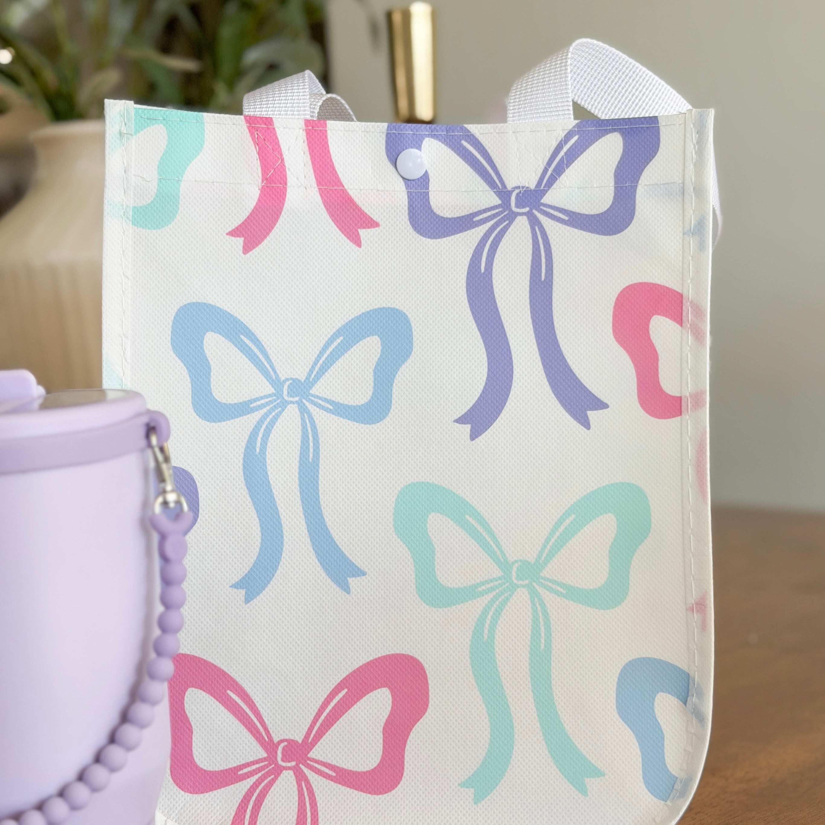 White tote bag with colorful bow patterns next to a purple container.