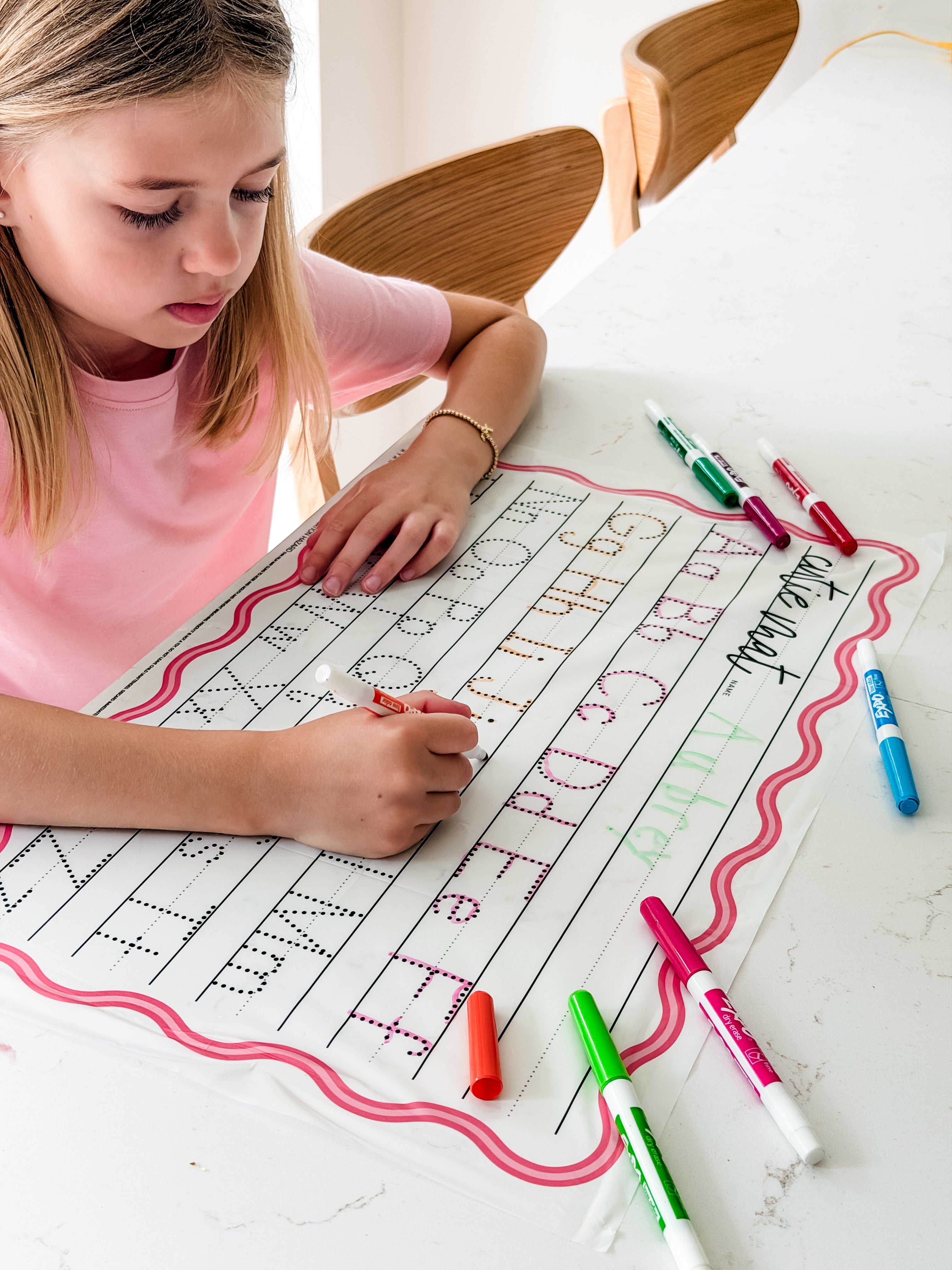 Child writing on a worksheet with markers on a white surface