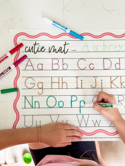 Child writing on a cutie mat with alphabet tracing lines and colorful markers.