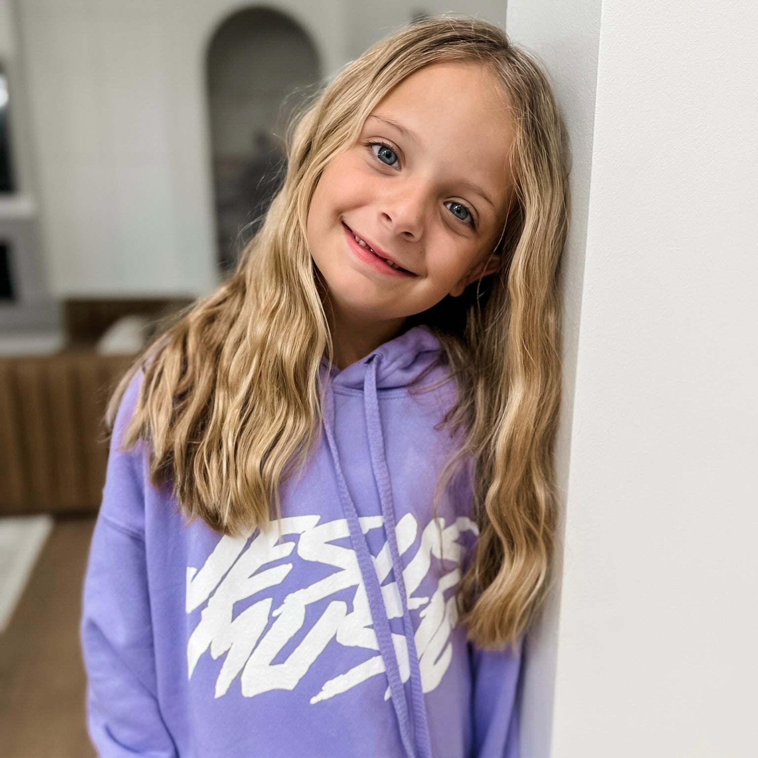 Young girl wearing a purple hoodie with a white logo indoors
