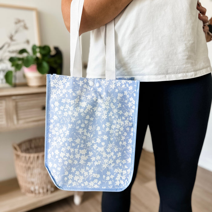 Person holding a blue floral-patterned tote bag indoors