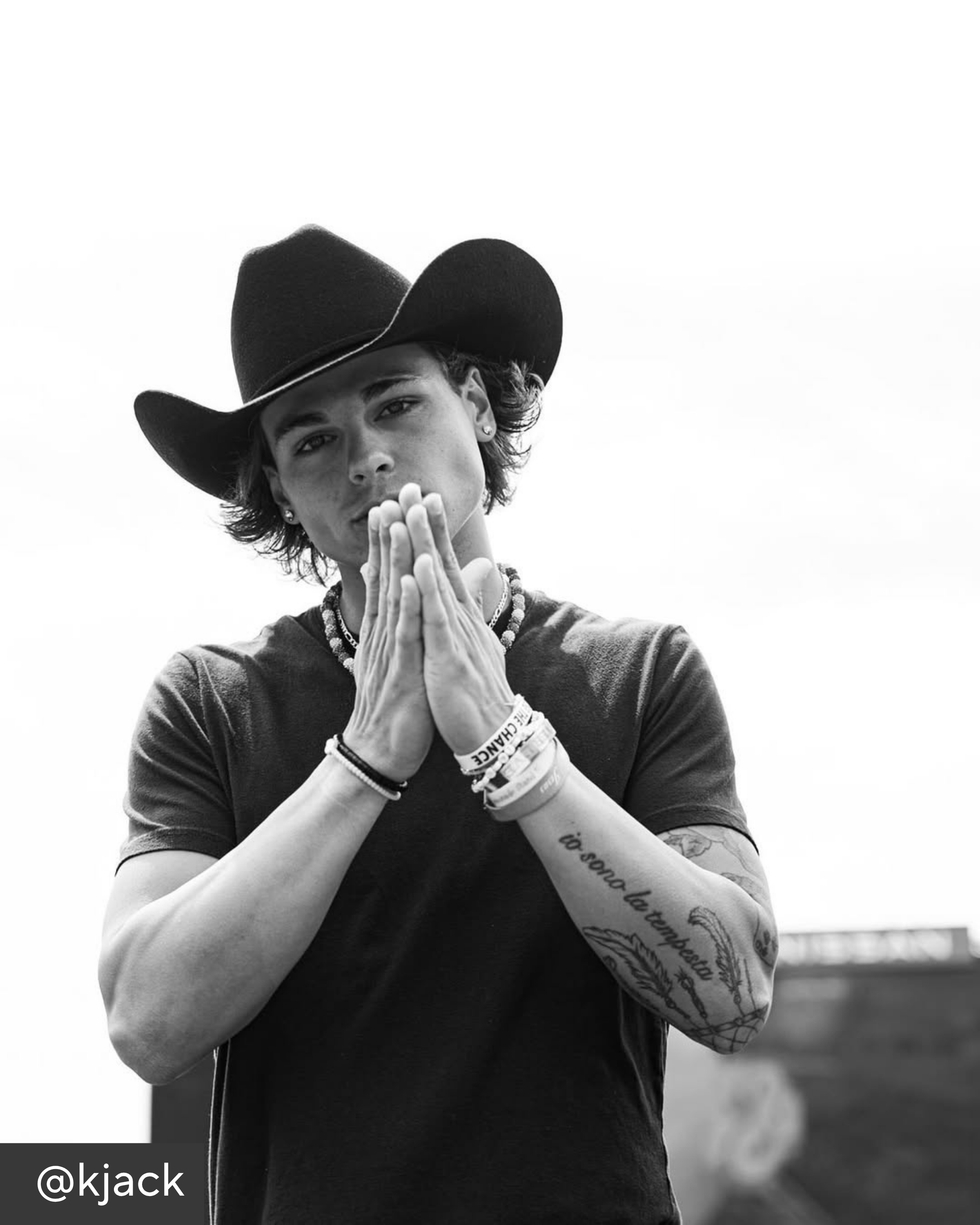 Person wearing a cowboy hat with hands pressed together in a black and white photo.
