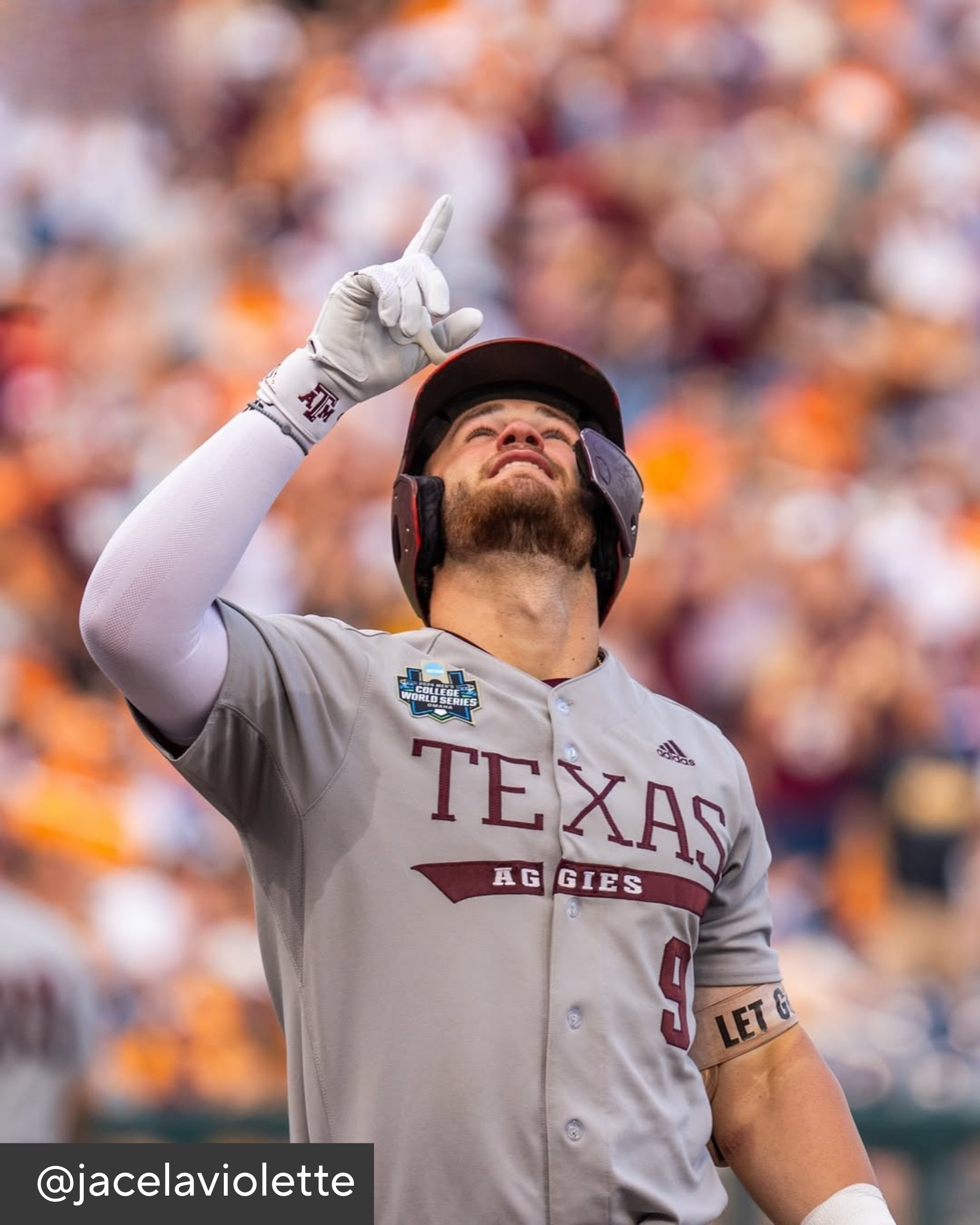 Baseball player in Texas Aggies uniform pointing upwards with a blurred crowd in the background
