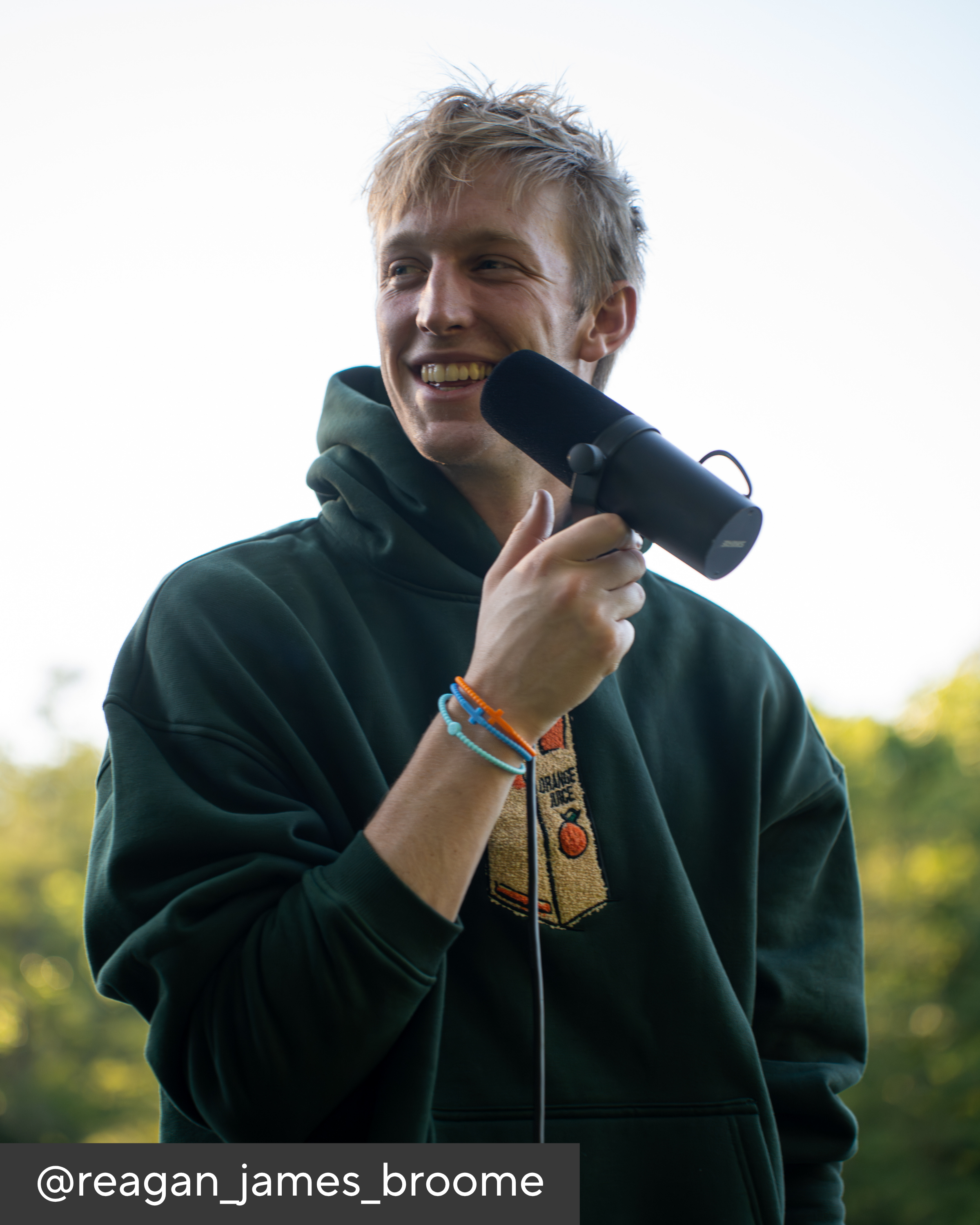 Person holding a microphone outdoors with a blurred natural background