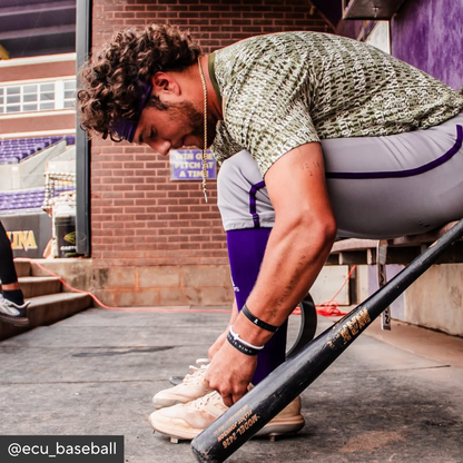 Person adjusting a baseball bat on a wooden surface with a stadium in the background