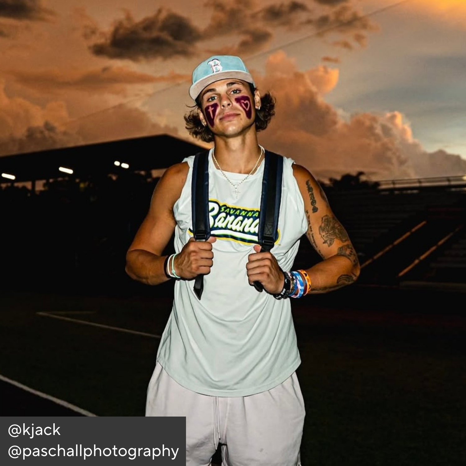 Person with suspenders and tattoos against a sunset sky