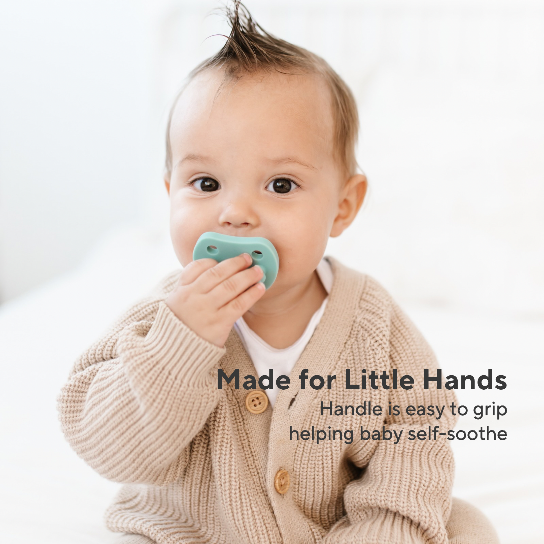 A baby wearing a beige knit cardigan holds a mint green pacifier against their mouth. Text on the image reads &