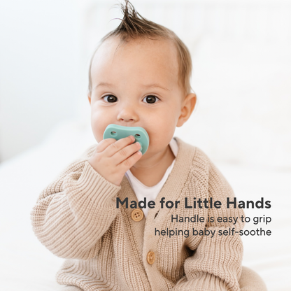 A baby wearing a beige knit cardigan holds a mint green pacifier against their mouth. Text on the image reads &