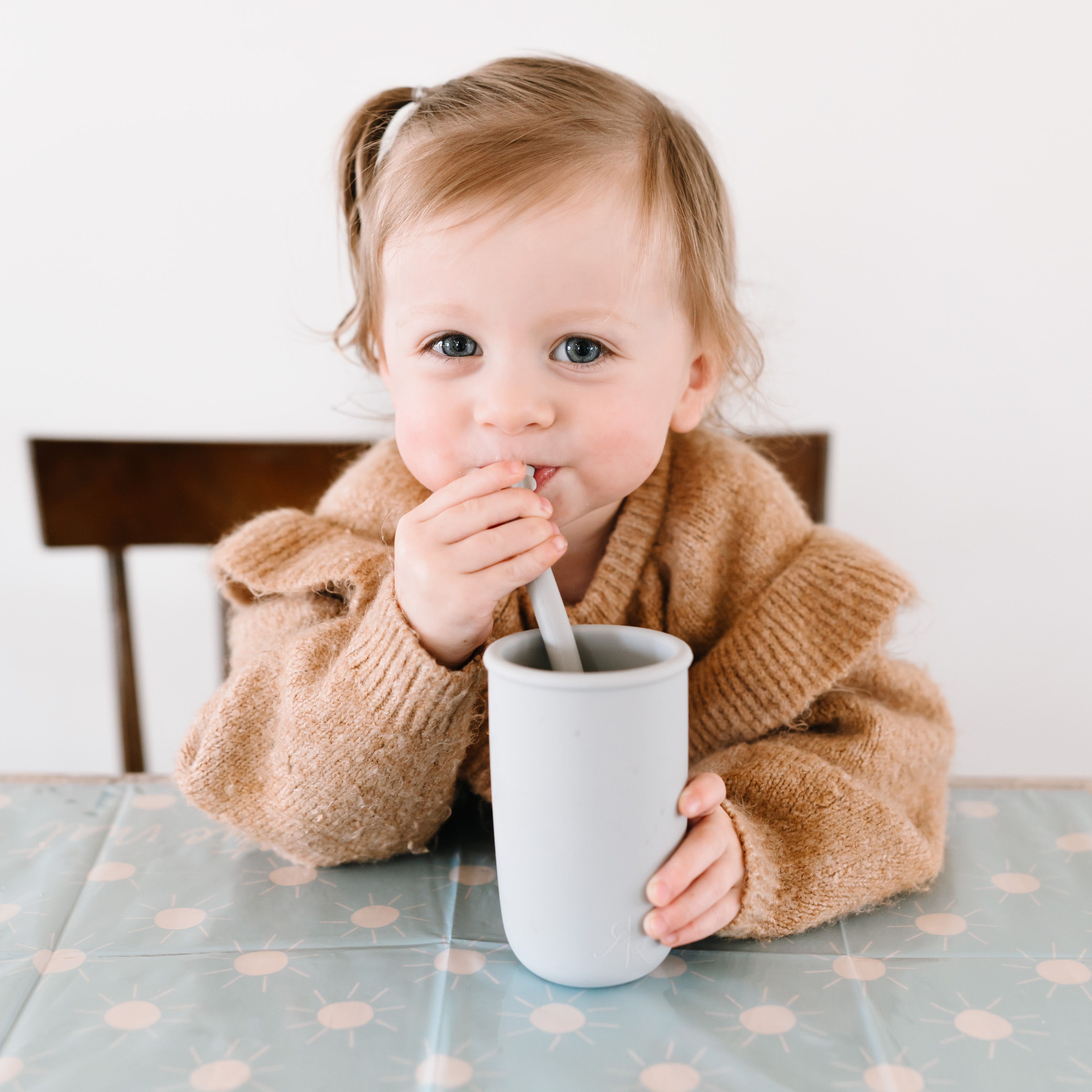 Toddler sitting at the table using the Cutie Cup and Shark Cutie Straw.