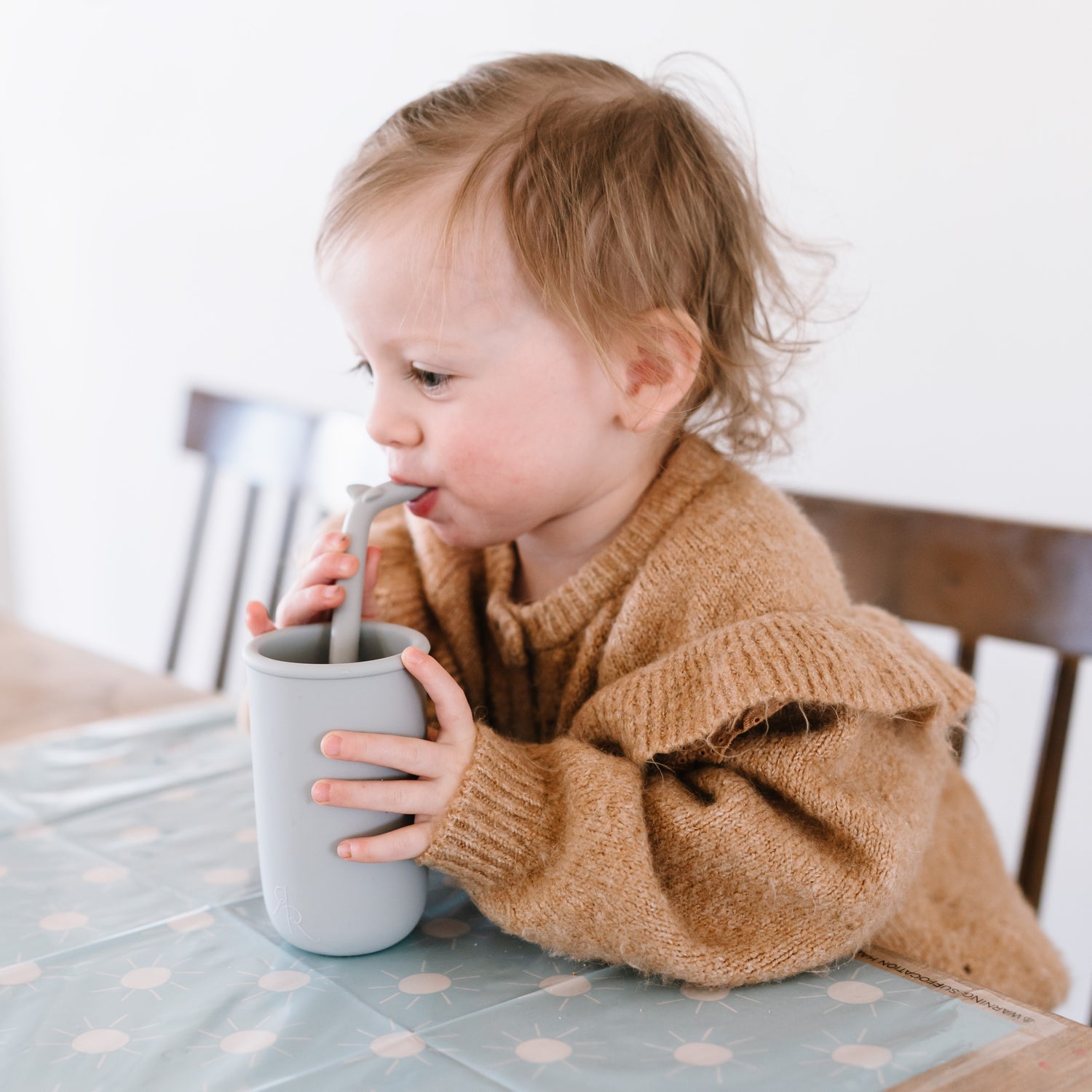 Toddler sitting at the table using the Cutie Cup and Shark Cutie Straw.