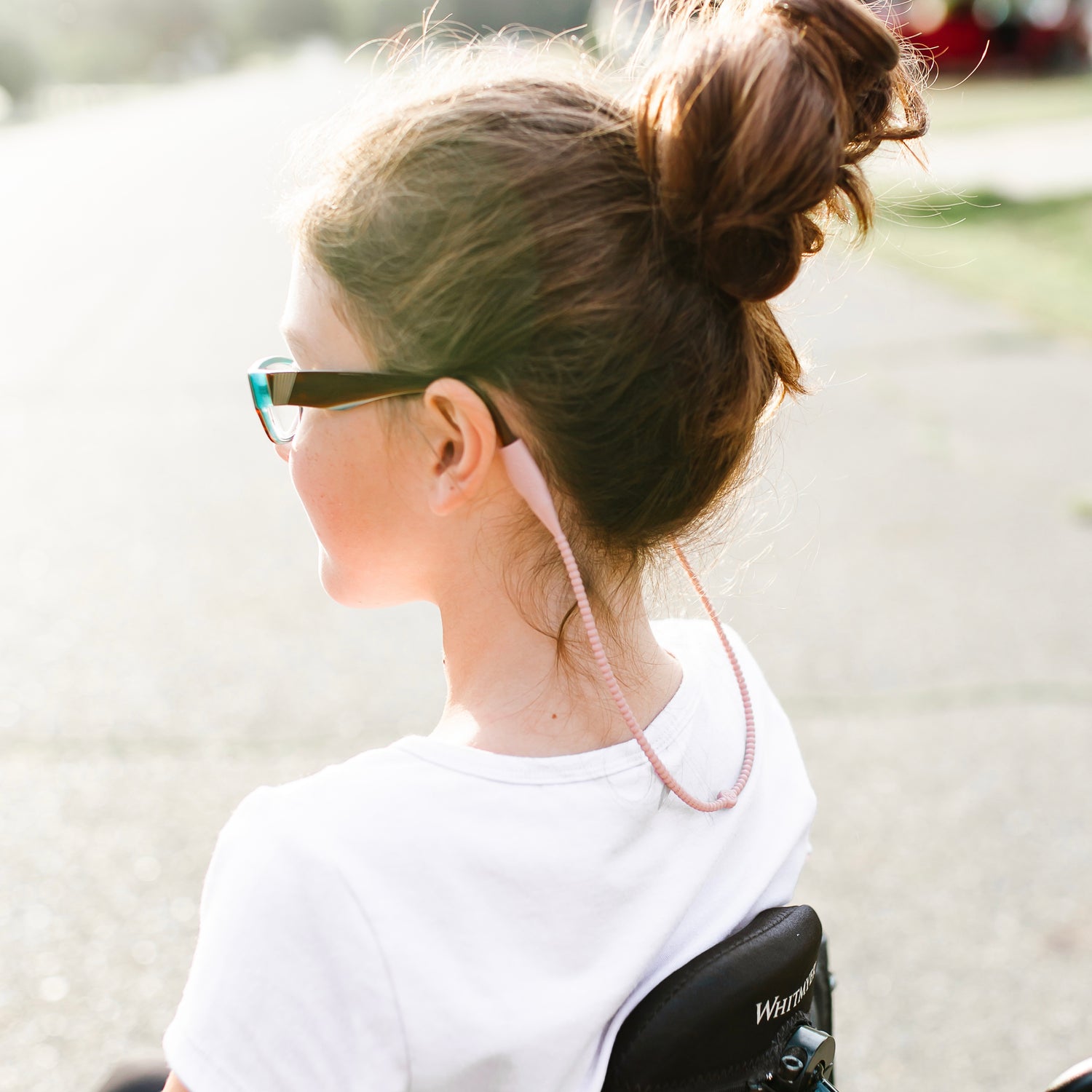 Girl in a wheelchair wearing the Hazel Cutie Straps attached to her glasses.