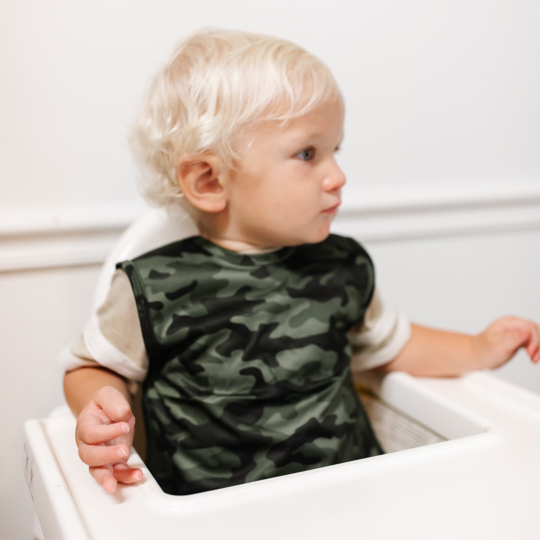 Baby sitting in a high chair wearing the Camo Cutie Bapron.